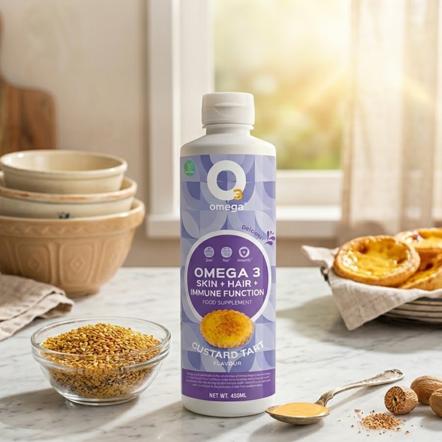 A bottle of O3Omega Skin, Hair, and Immune Function liquid food supplement in Custard Tart flavour, displayed on a kitchen counter with a bowl of flaxseeds and fresh custard tarts.